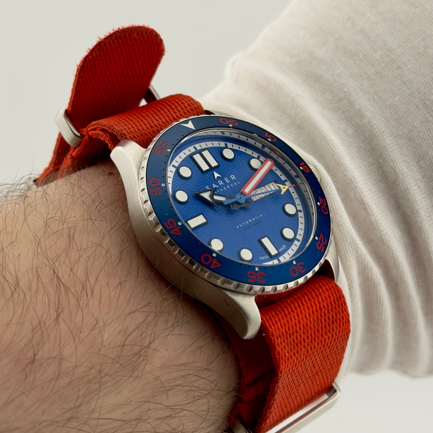 Wrist wearing a watch with a blue face and red strap on a light background