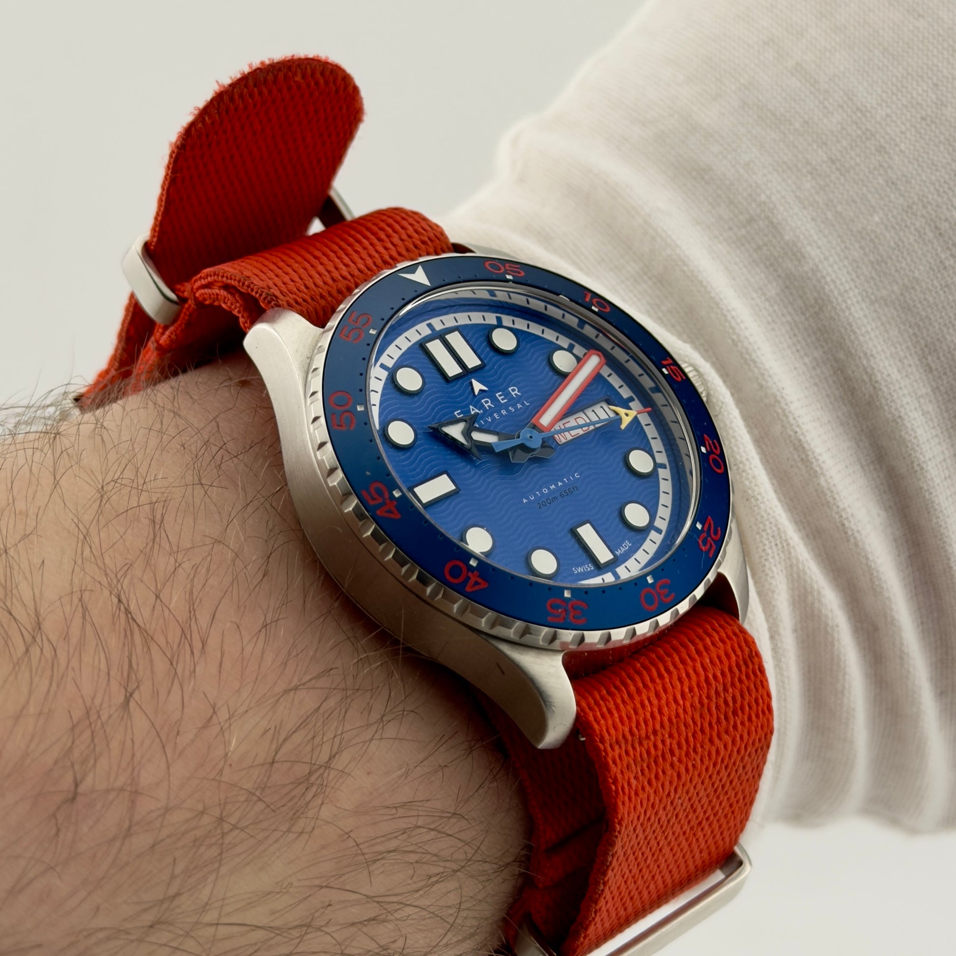 Wrist wearing a watch with a blue face and red strap on a light background