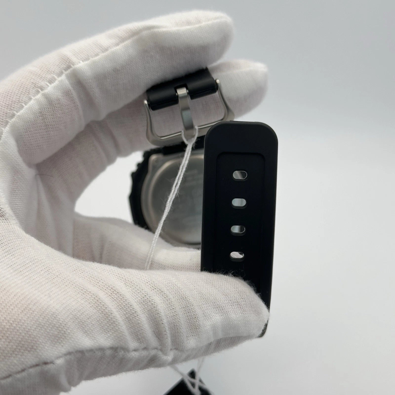 Black watch strap being adjusted by a gloved hand on a light gray background