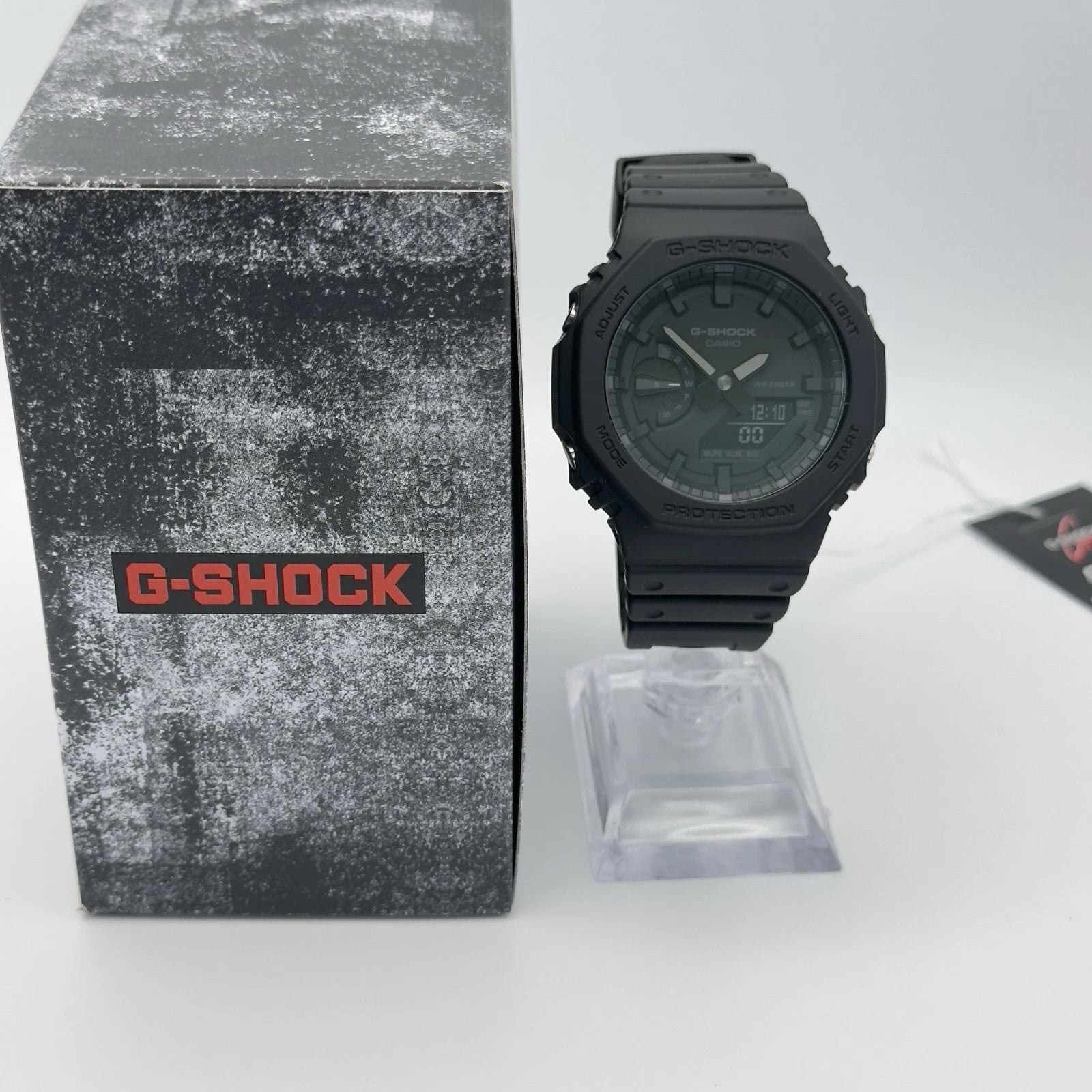 Black G-Shock watch next to its packaging on a white background