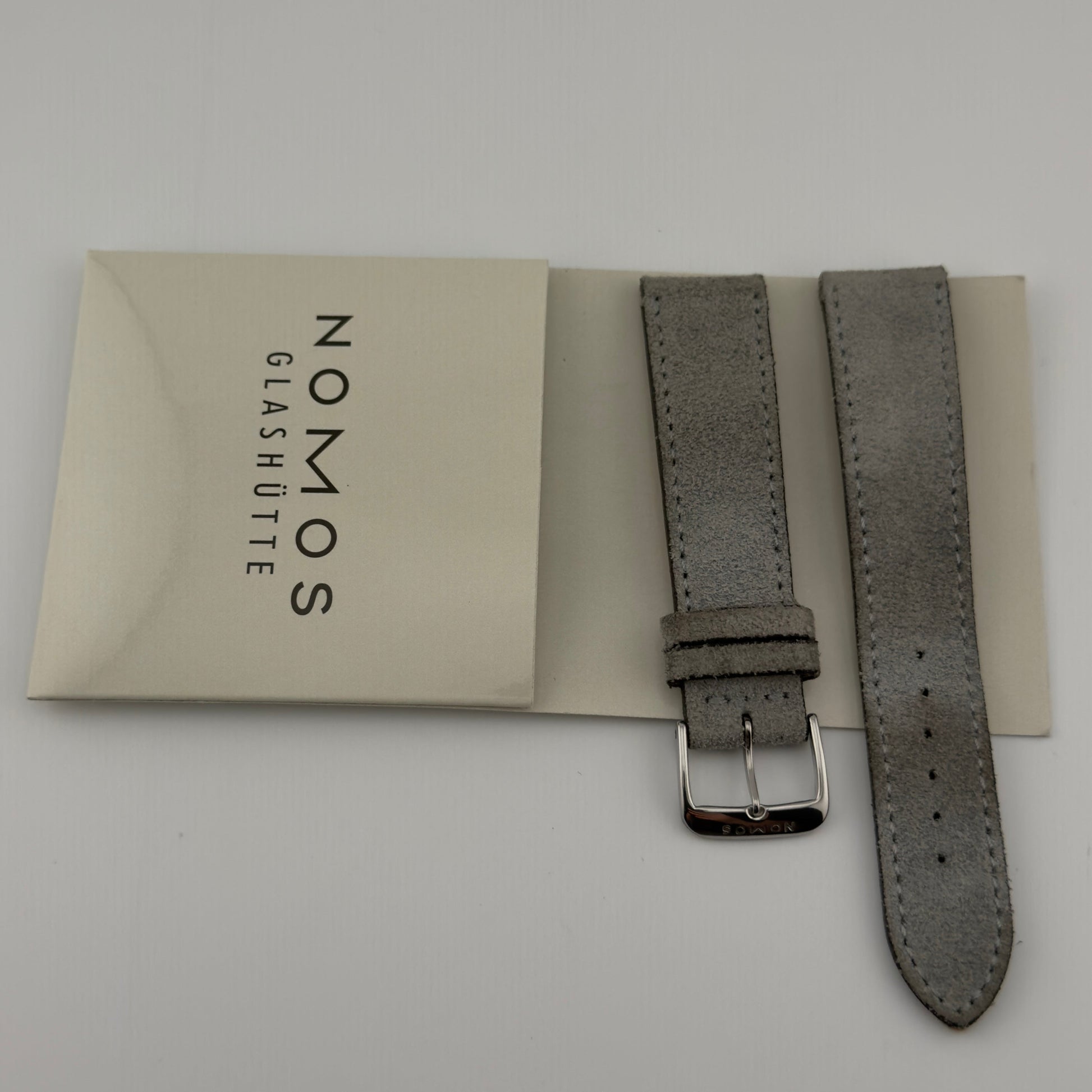Gray watch strap with Nomos Glashüte packaging on a light gray background