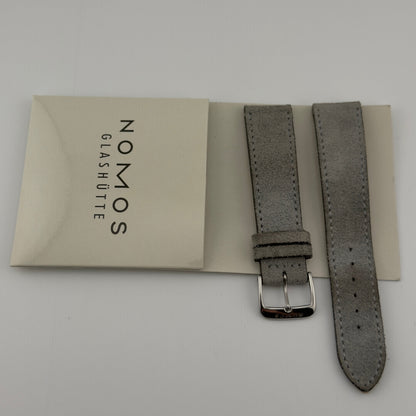 Gray watch strap with Nomos Glashüte packaging on a light gray background