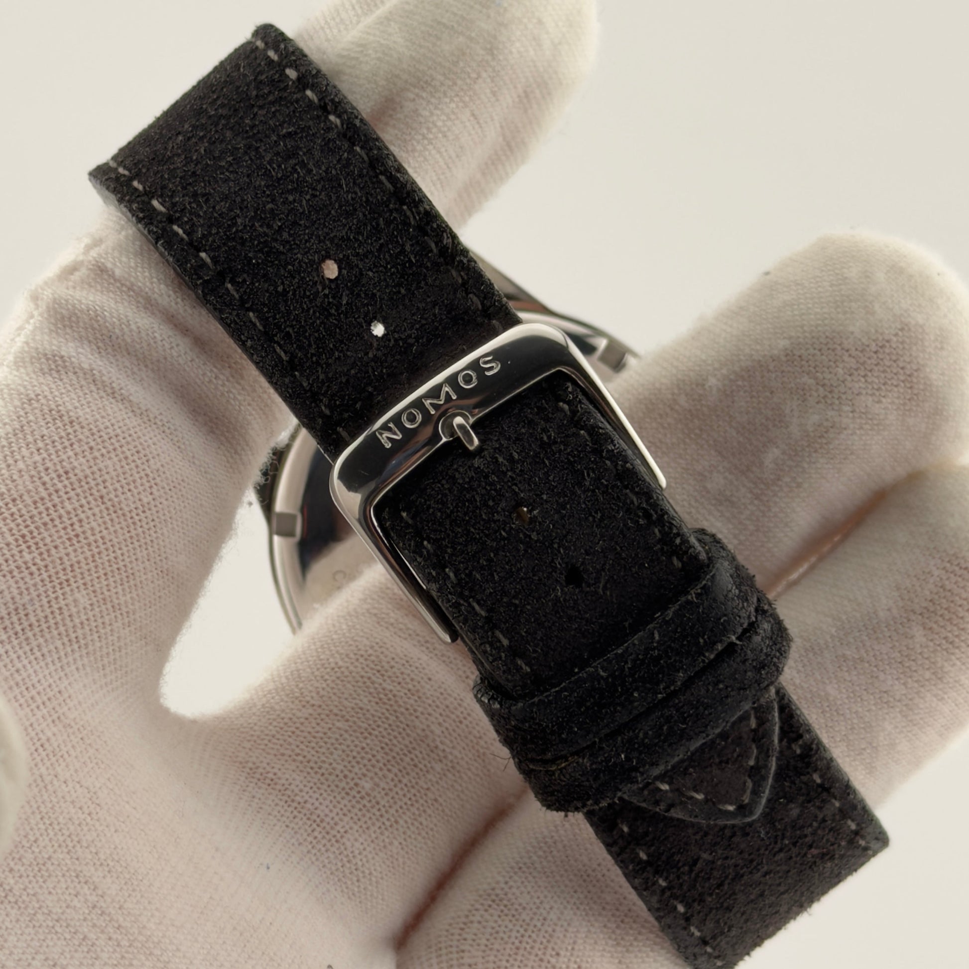 Black watch strap with 'Nomos' branding on a light fabric background