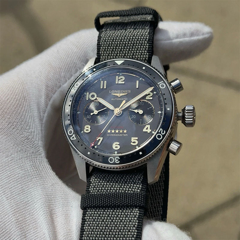 Longines watch with black strap held by a gloved hand on a neutral background