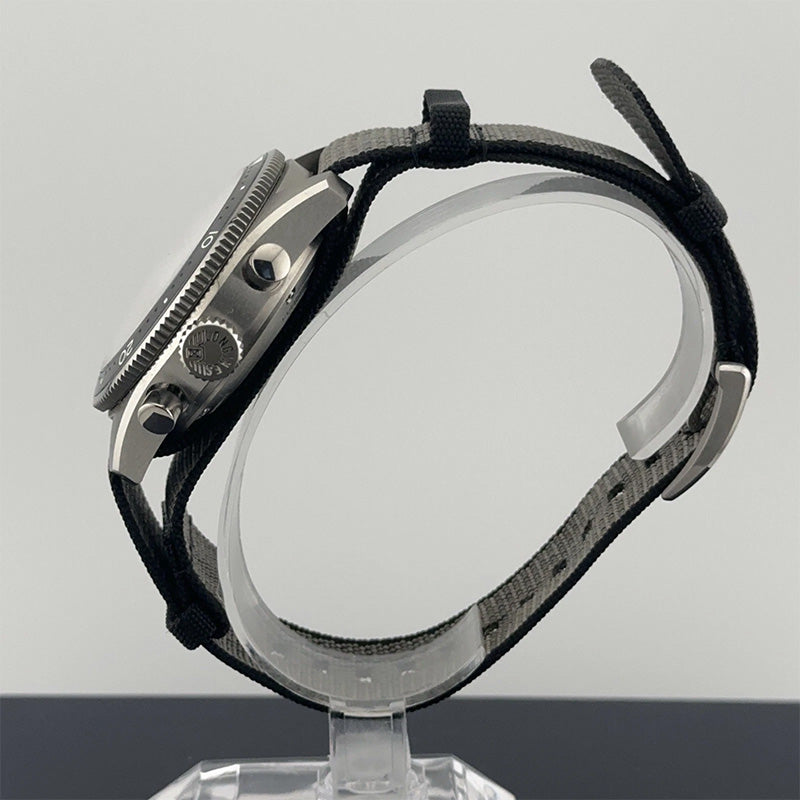 Watch with black strap on a clear stand against a gray background