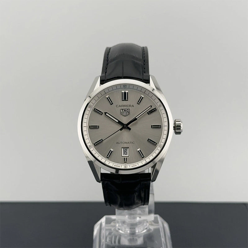 A TAG Heuer Carrera watch with a grey dial, steel case, and black leather strap, photographed against a neutral background with a reflection visible below.